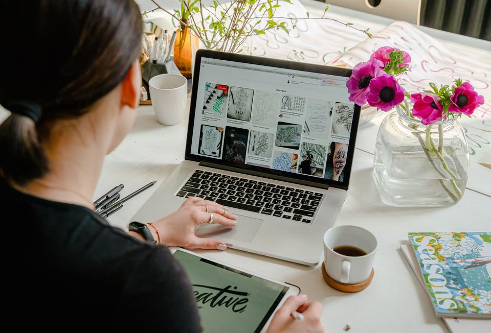 Mujer revisando referencias de lettering en su laptop mientras dibuja en una tableta