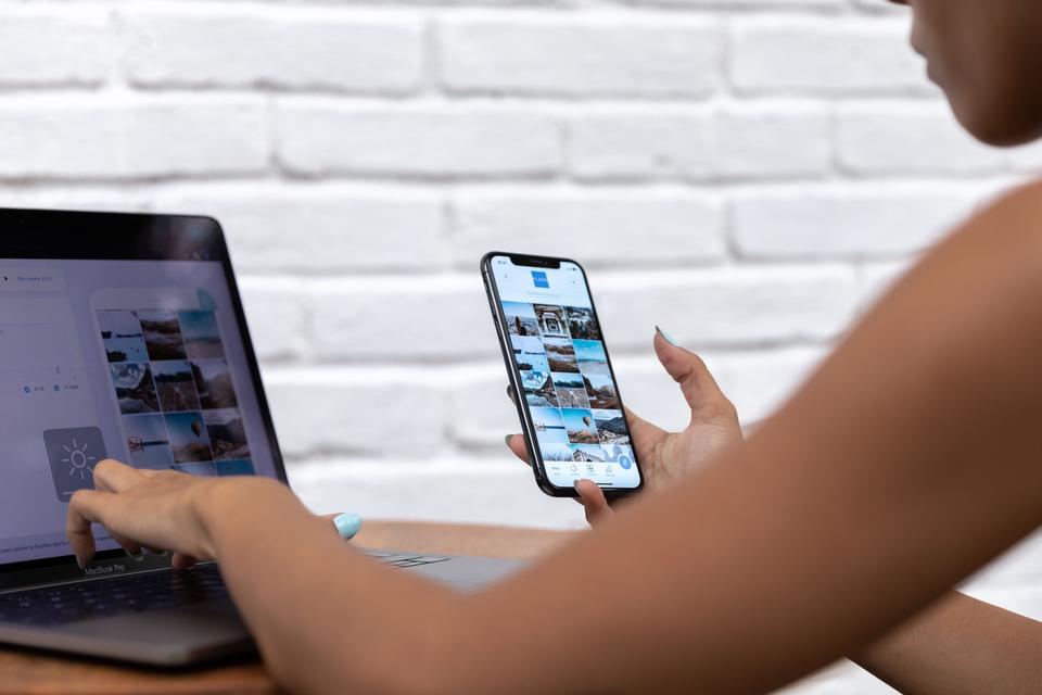 Persona revisando en su celular la cuadrícula de publicaciones de una cuenta, junto a su laptop